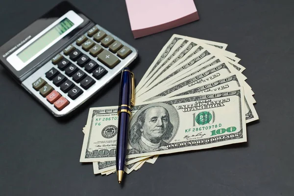 Dollars américains sur table de bureau noire avec calculatrice et ordinateur portable — Photo