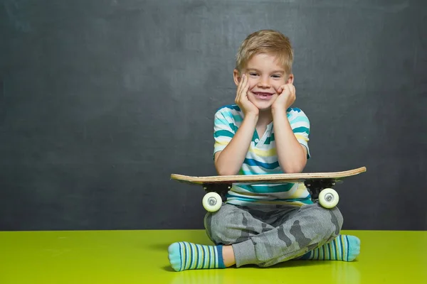 学校の男の子は、彼の後ろの黒板のスケート ボードと立っています。 — ストック写真