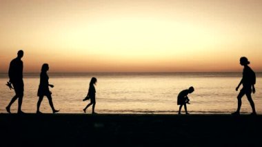Aile silueti gün batımında sahilde yürüyor.