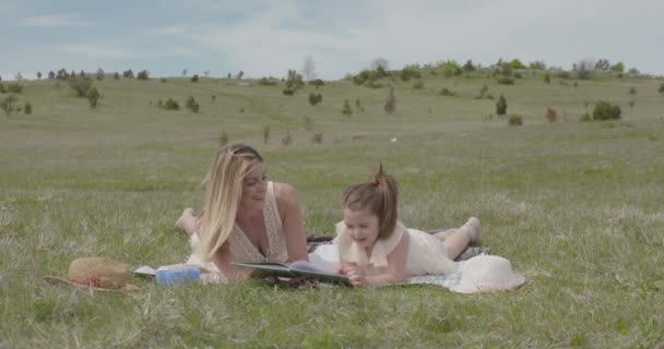 若い美しい母親と彼女の娘は自然公園で楽しみ 本を読む — ストック動画