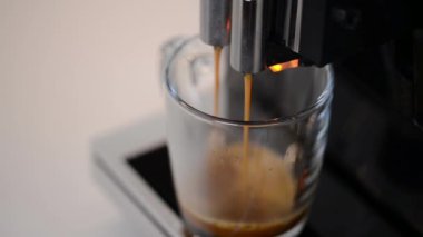 Modern kahve makinesinden sade kahve yapma sürecinin yakın çekimi, berrak cam bardağa döküldü. Kahve makinesi köpüklü taze espresso yapıyor..