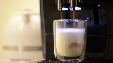Modern kahve makinesinden latte kahve yapma sürecinin yakın çekimi, berrak cam bardağa döküldü. Kahve makinesi sütlü sıcak latte macchiato yapıyor..