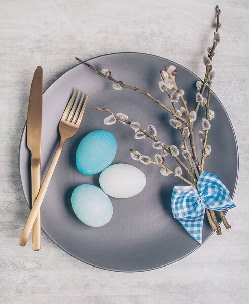 Easter table setting with grey plate and blue eggs on grey wooden table. 
