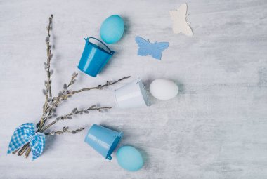 Mavi Paskalya yumurtası ve söğüt dalları mavi kurdeleyle bağlanmış ve gri ahşap bir masada küçük kovalarla.. 