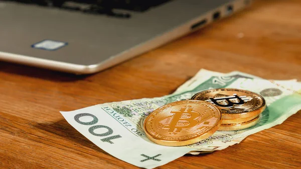 Goldener Bitcoin mit Papierwährung. Internet-Kryptowährungskonzept. physische Version des virtuellen Geldes. — Stockbild Eine symbolische Münze aus Bitcoins auf polnische Zloty-Banknoten, Laptop im Hintergrund. Bitcoin-Bargeld in Zloty umtauschen. — Stockfoto