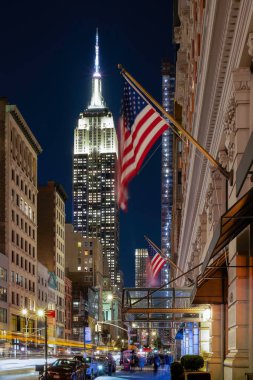Günbatımında New York City 'de trafik, insan ve bayrak bulunan Empire State binasının sokak manzarası