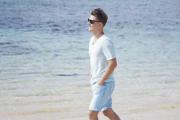 Homme en lunettes de soleil marchant à la plage — Photo