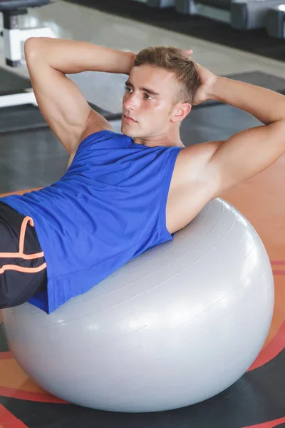 Человек делает сидеть на шаре упражнений — стоковое фото