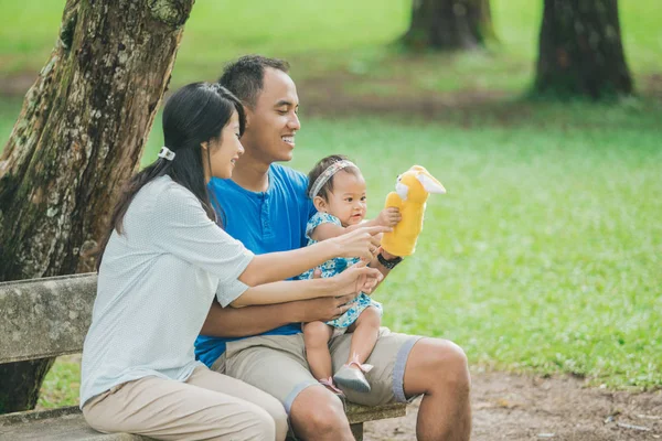 Gelukkige familie zittend op een bankje in het park en het spelen met han — Stockfoto