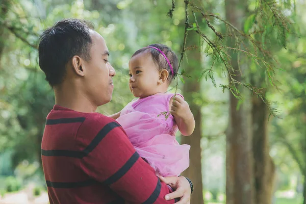 Ojciec posiada małą córeczkę w ramionach wśród drzew — Zdjęcie stockowe