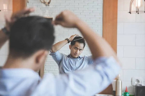 Homem penteando seu cabelo depois de ter um corte na barbearia — Fotografia de Stock