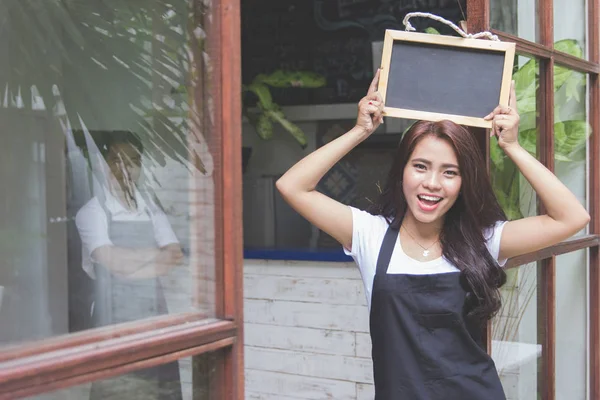 Trabajadora de cafetería sonriendo y sosteniendo pizarra en blanco —  Fotos de Stock