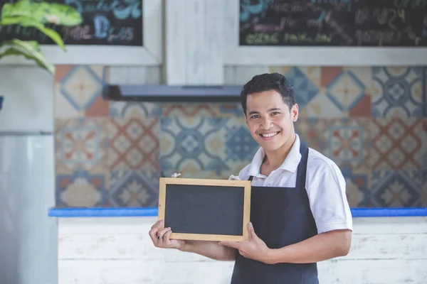 Manliga café arbetare leende och hålla tomt blackboard — Stockfoto