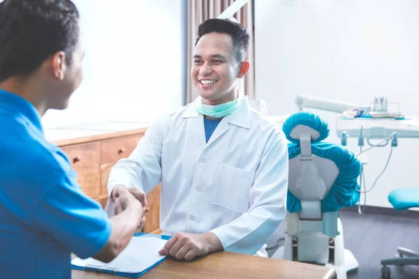 Tandläkare att prata med sin patient på tandvård klinik och skakar — Stockfoto