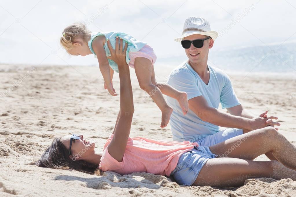 young parents playing with their little daughter at the beach