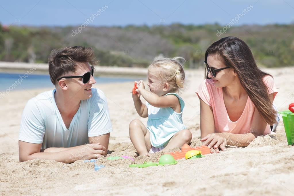 joyful little family lying on sand at the beach