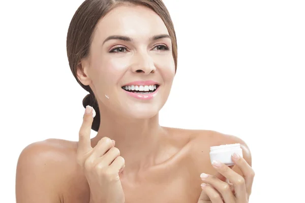 Hermosa mujer aplicando un poco de crema facial mientras sonríe —  Fotos de Stock