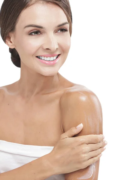 Beautiful woman applying body lotion to her arms while smiling — Stock Photo, Image