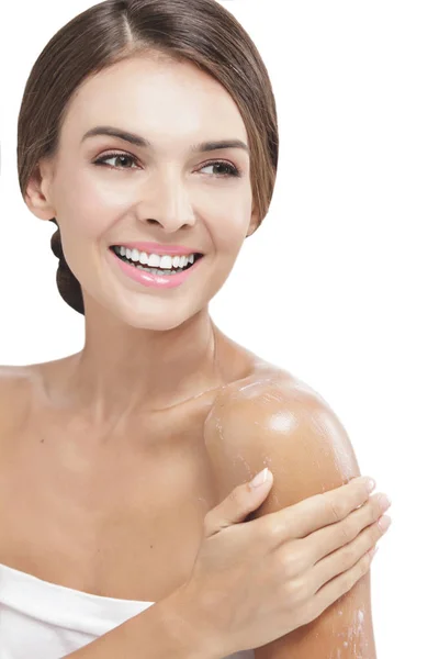 Beautiful woman applying body lotion to her arms while smiling — Stock Photo, Image