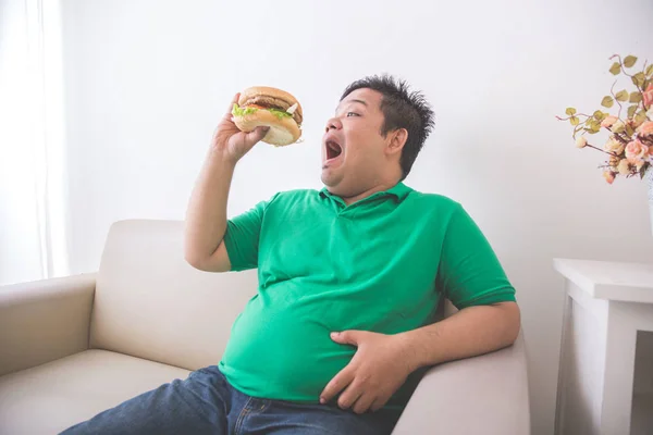 Homme en surpoids manger un hamburger à la maison — Photo