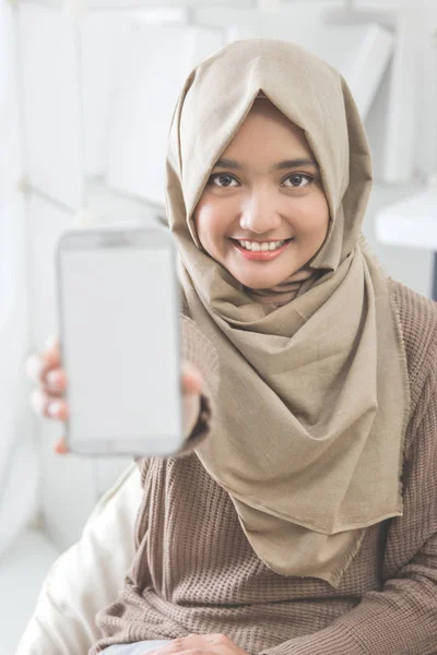Женщина показывает экран мобильного телефона и улыбается в камеру — стоковое фото