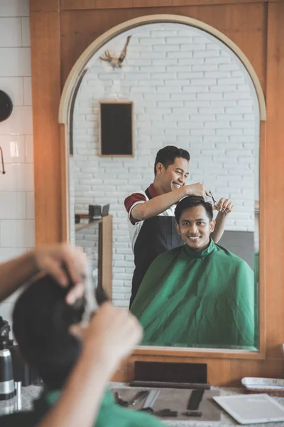 man getting haircut by hairdresser at barbershop