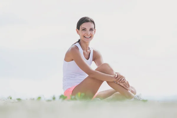 Здорова спортивна жінка посміхається, сидячи на землі — стокове фото