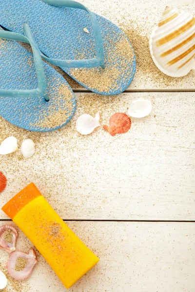 Blue flipflops, sunblock, and seashells on white wooden table — Stock Photo, Image