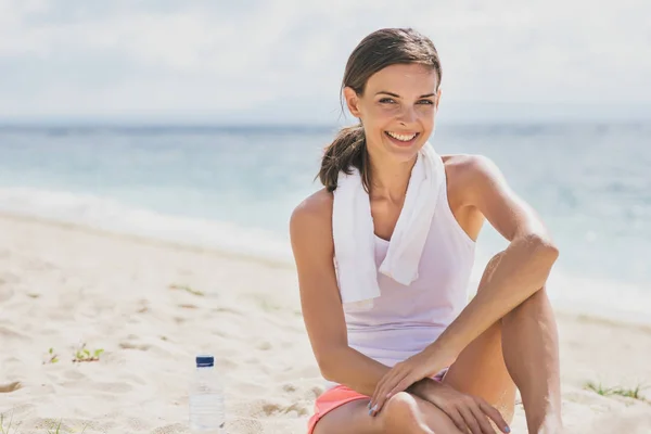 Donna sportiva sorridente mentre seduto sulla sabbia — Foto Stock