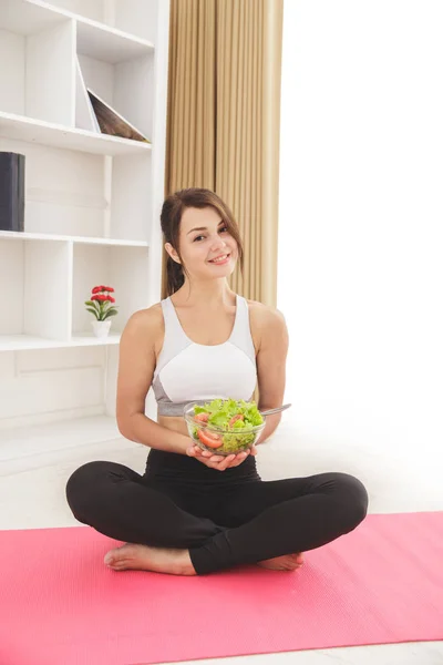 Gesundes, sportliches Mädchen sitzt, während es eine Schüssel Salat in der Hand hält — Stockfoto