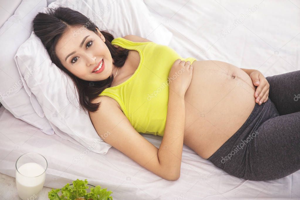 healthy pregnant woman smiling while lying on bed