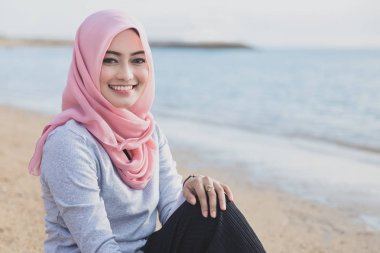 plajda otururken gülümseyen hijab giyen güzel kadın