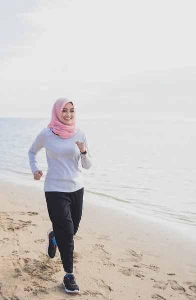 Sportowy kobieta noszenie hidżabu uśmiechający się podczas joggingu na plaży — Zdjęcie stockowe