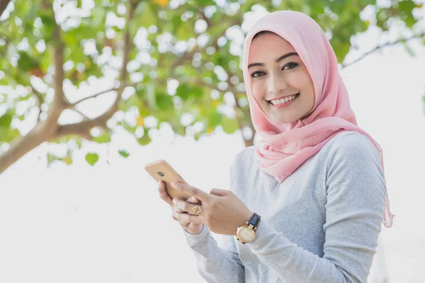 Красивая женщина в хиджабе улыбается, когда пишет смс на мобильнике — стоковое фото