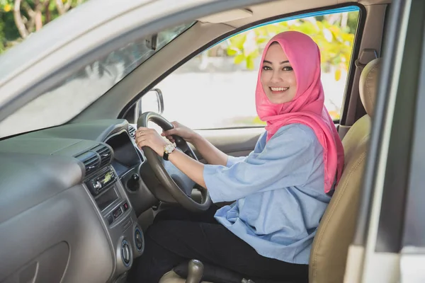 beautiful woman wearing hijab smiling while driving a car