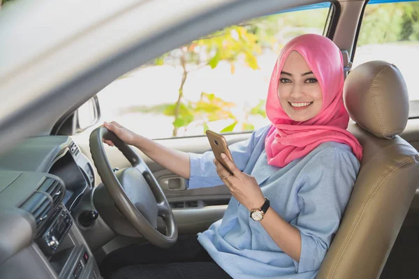 Красивая женщина в хиджабе держит смартфон во время вождения — стоковое фото
