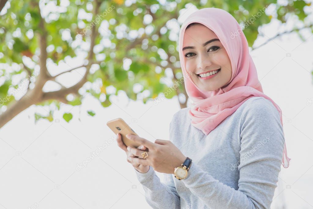 beautiful woman wearing hijab smiling while texting on mobilepho