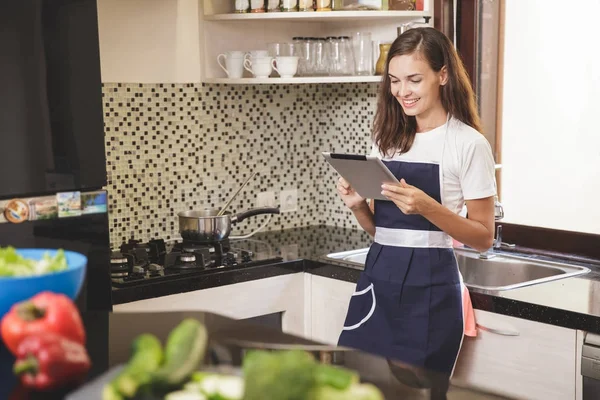 Mujer leyendo en la tableta mientras cocina —  Fotos de Stock