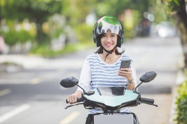 Motosiklet üzerinde akıllı telefon kullanan kadın