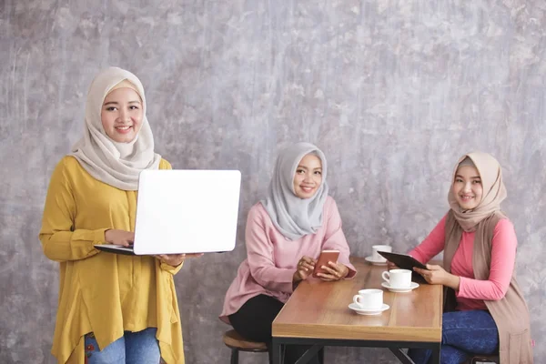 beautiful muslim woman smiling and standing while holding laptop