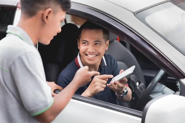 Водитель показывает свой мобильный телефон мужчине, стоящему рядом с его машиной — стоковое фото