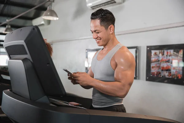 Asiático muscular hombre en cinta de correr celebración de teléfono inteligente — Foto de Stock