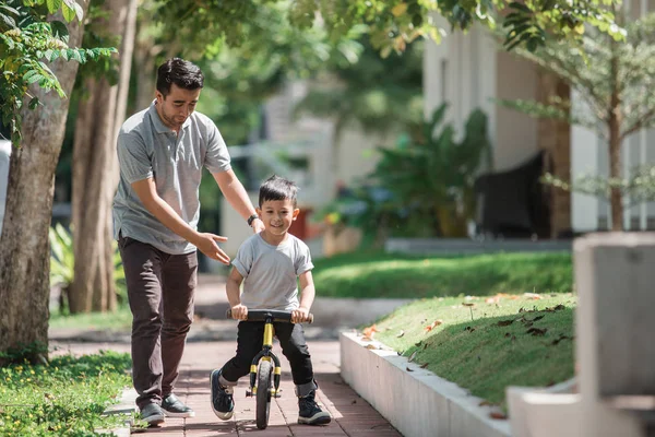 Kids ride bicycle push by his father — Stock Photo, Image