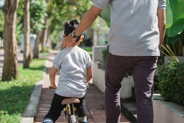 Kinder fahren Fahrrad, das vom Vater geschoben wird — Stockfoto