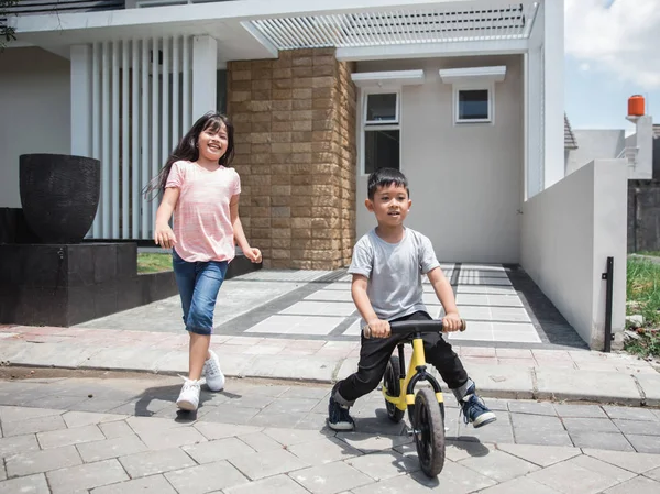 Anak-anak mengendarai sepeda dan adik berjalan di belakangnya — Stok Foto