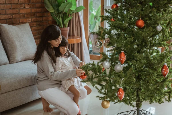 mother and daughter hanging some accessories on christmas tree