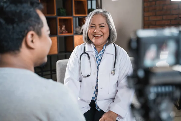 Uśmiechnięty lekarz rozmawiający z pacjentem i nagrywający kamerą — Zdjęcie stockowe