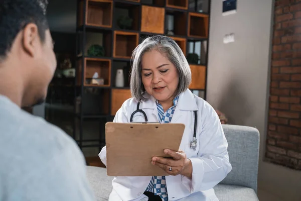 Die Ärztin macht sich Notizen mit dem Klemmbrett, wenn sie ihre Patienten fragt — Stockfoto