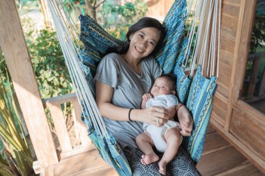 Asyalı anne hamakta dinlenirken bebeği tutuyor.