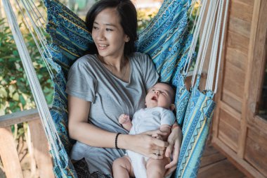 Anne hamakta dinlenirken kızını kucağına alıyor.